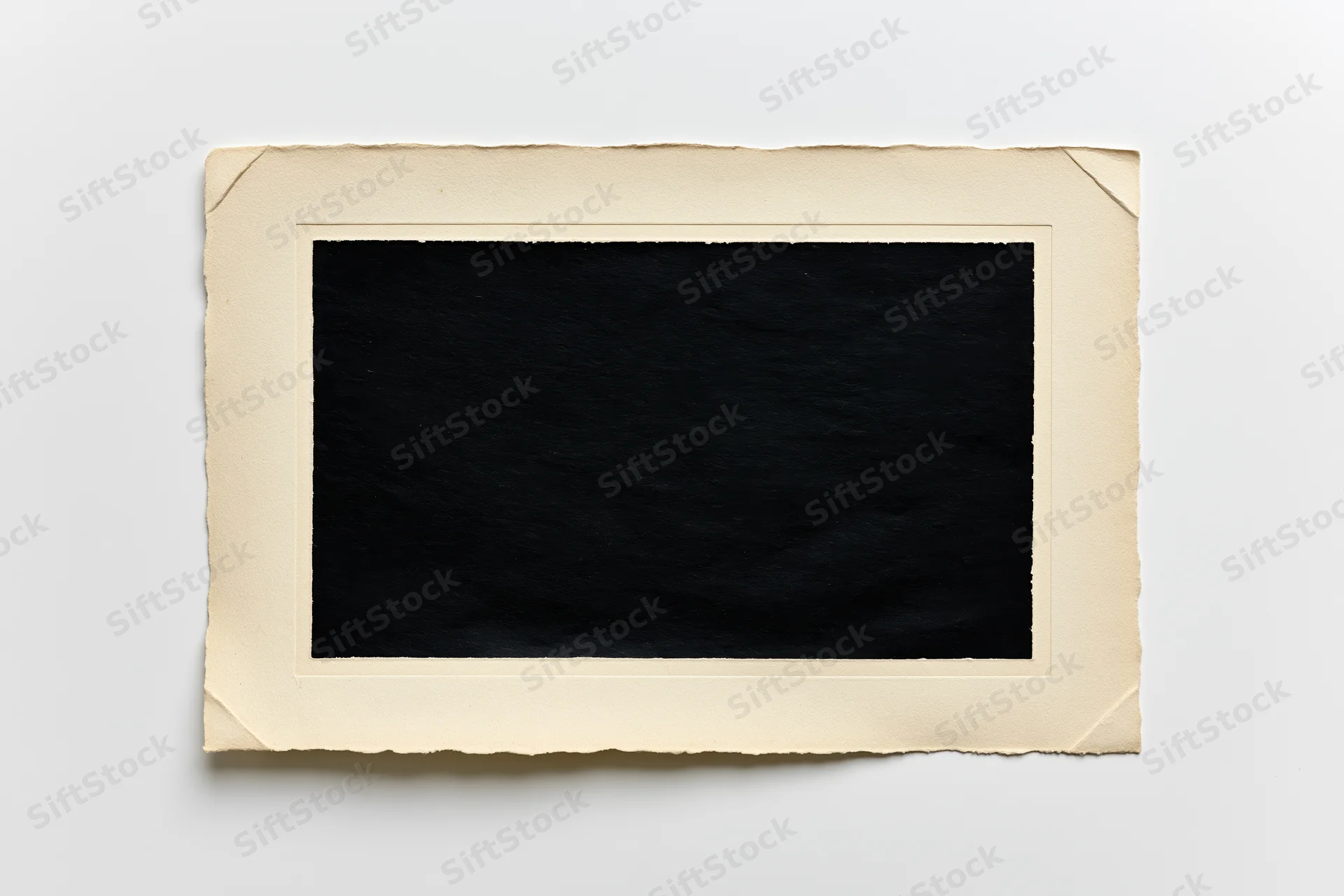 Vintage photo print with blank black center and torn beige border lying flat on white surface