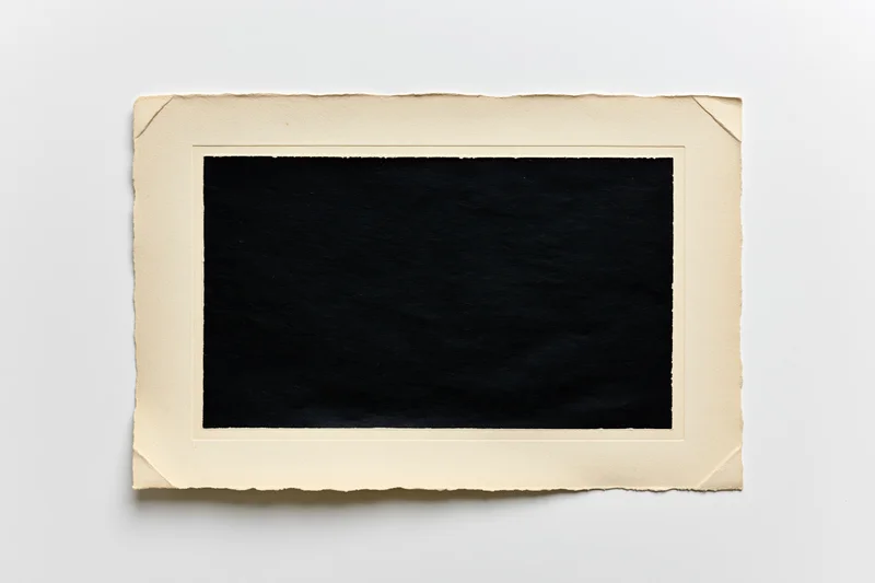 Vintage photo print with blank black center and torn beige border lying flat on white surface