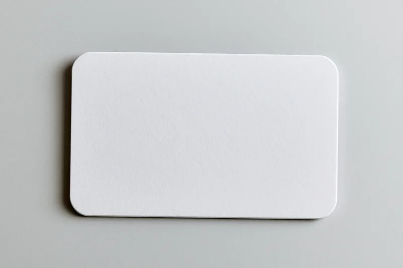 Blank white business card with rounded corners lying flat on gray surface