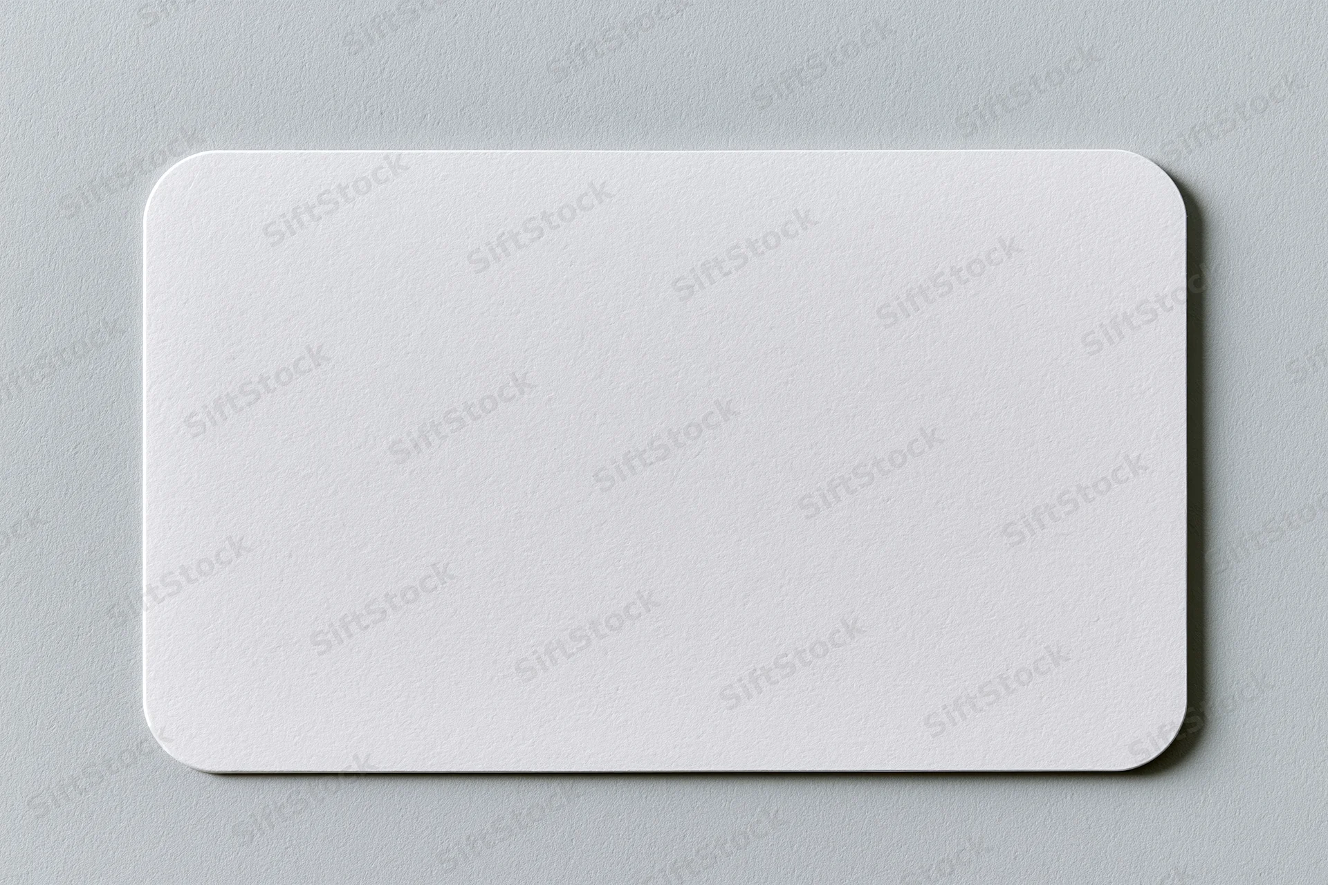 Blank white business card with rounded corners lying flat on gray surface