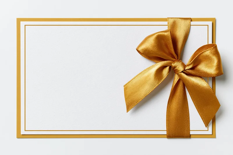 Blank white gift card with gold satin ribbon bow on plain surface