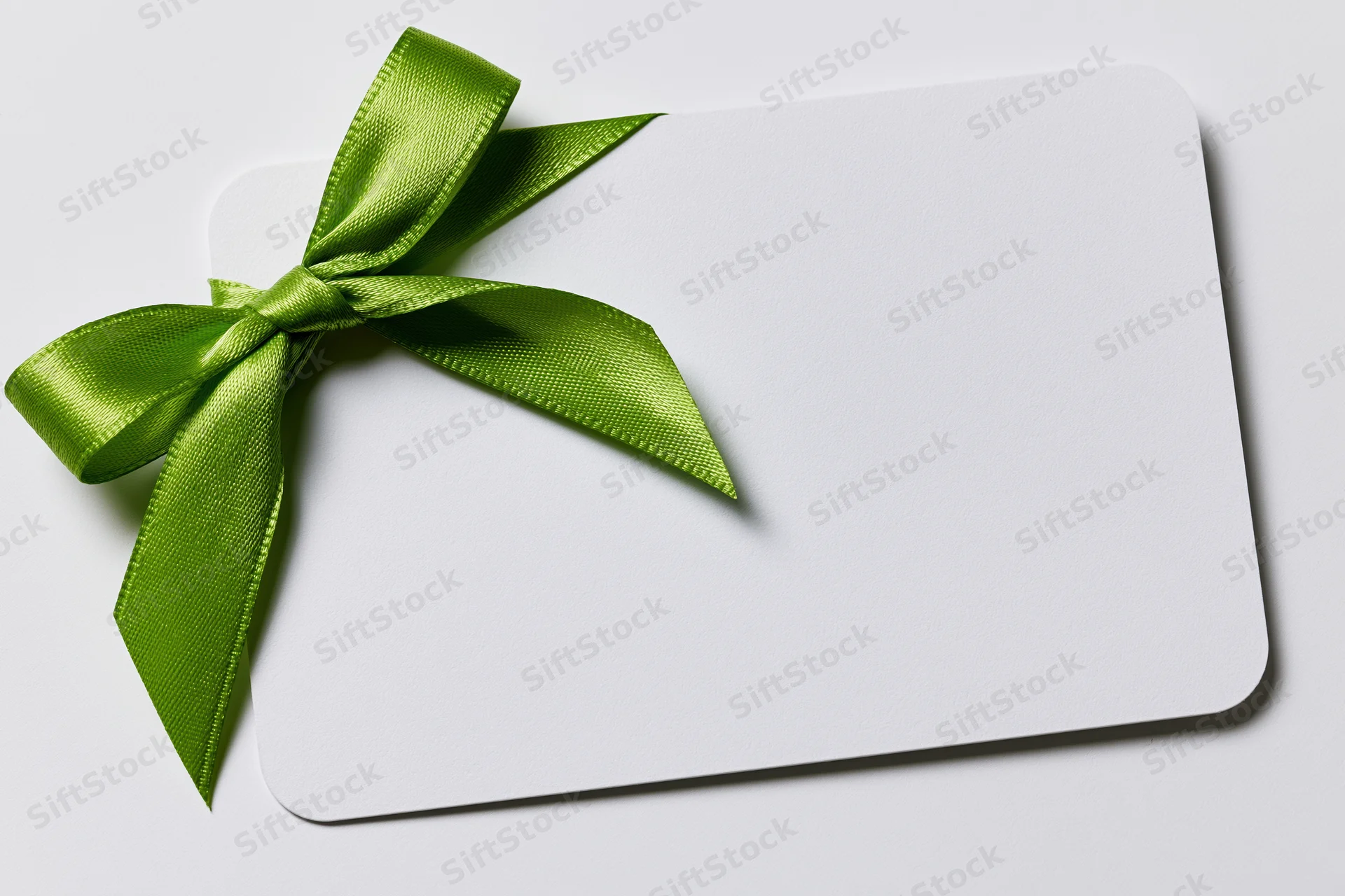 Blank white gift card with a green satin ribbon bow on plain surface