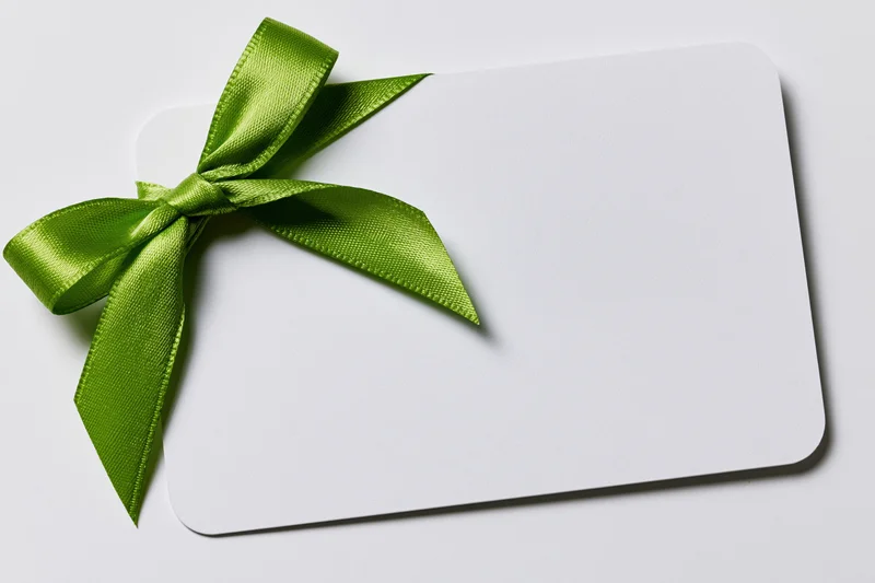 Blank white gift card with a green satin ribbon bow on plain surface