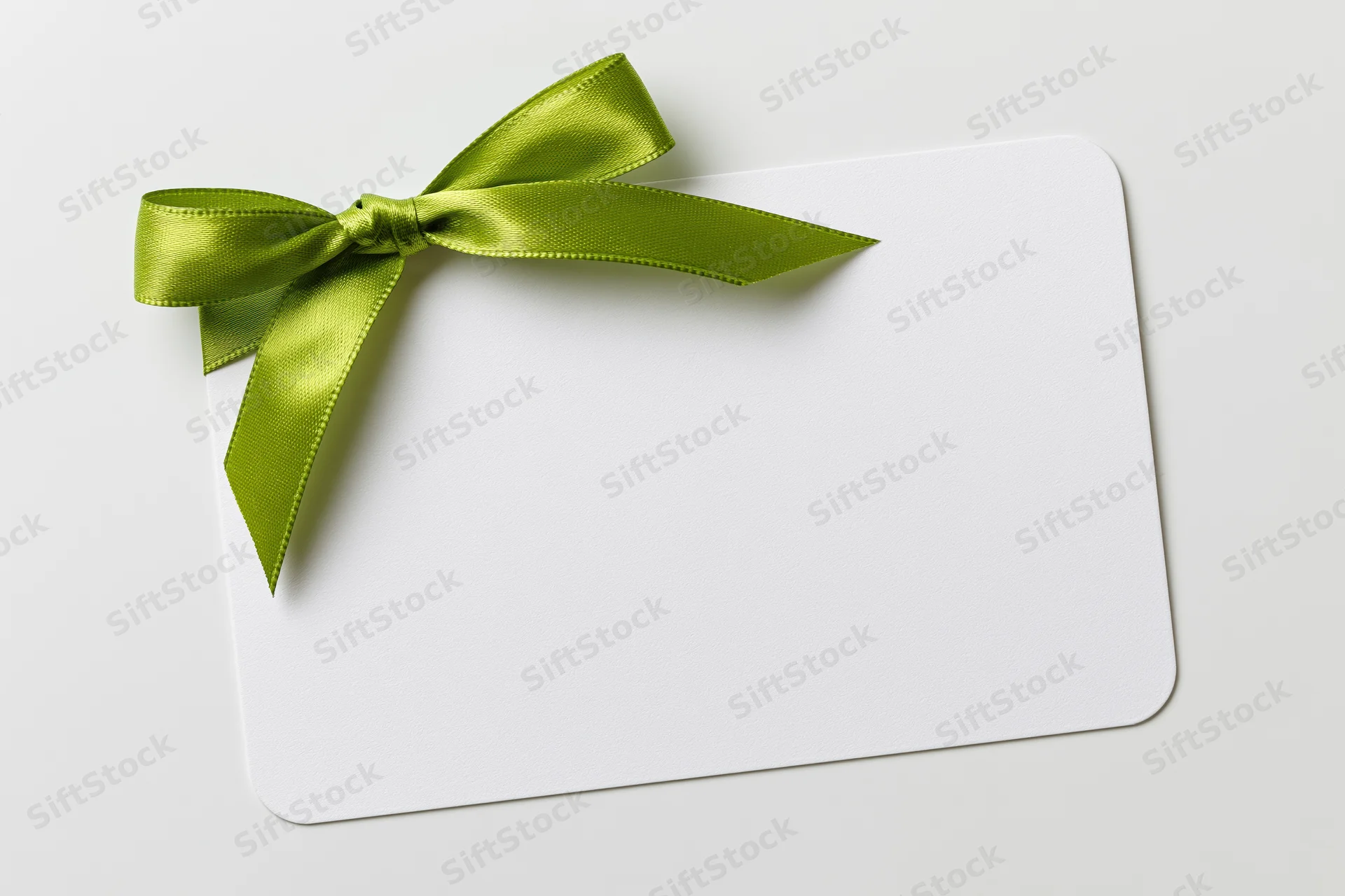 Blank white gift card with a lime green satin ribbon tied in a bow on a plain surface