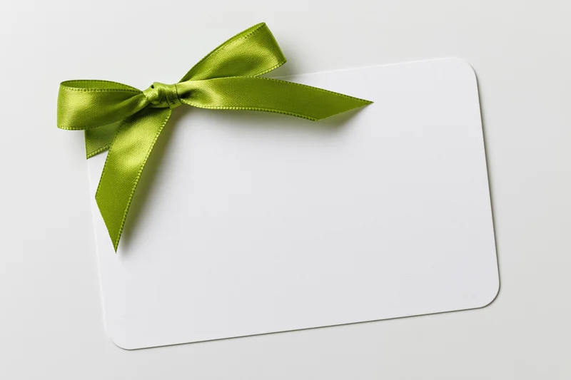 Blank white gift card with a lime green satin ribbon tied in a bow on a plain surface