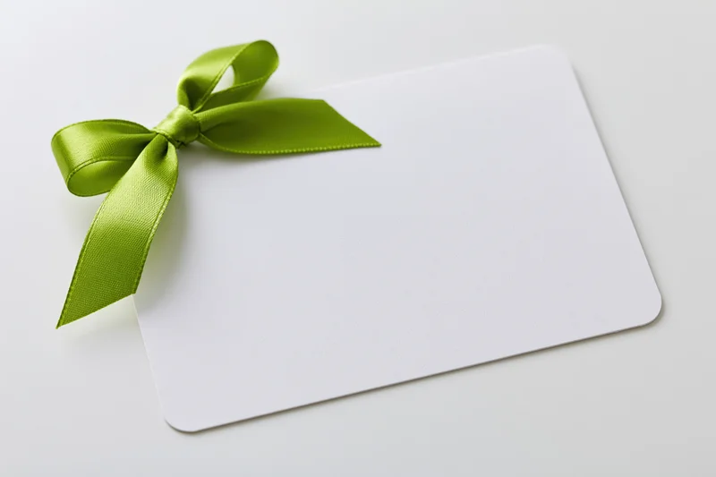 Blank white gift card with a lime green satin ribbon tied in a bow on a plain white surface