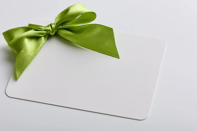 Blank white gift card with lime green satin ribbon bow on plain white surface