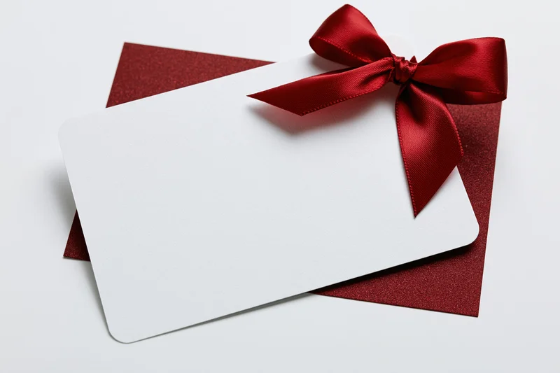 Blank white gift card with red ribbon bow on dark red envelope against white background