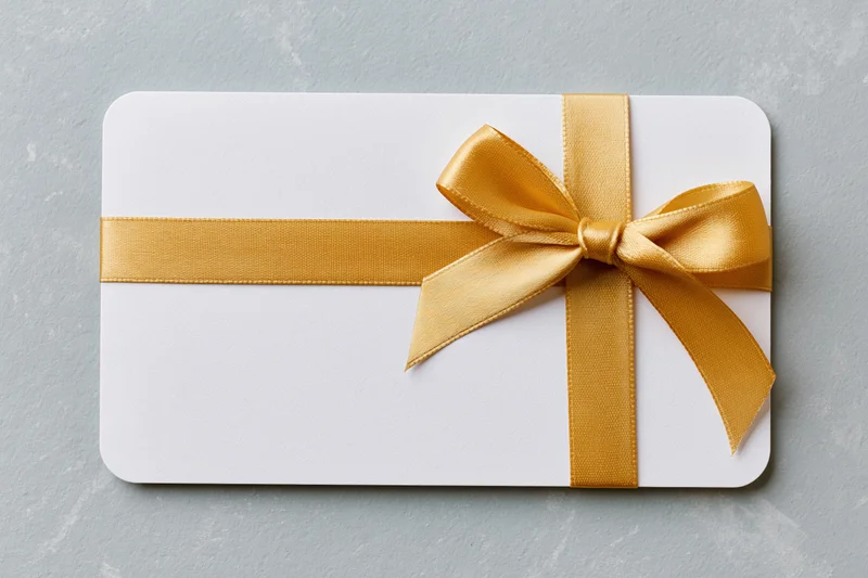 White gift card with gold ribbon bow on gray surface