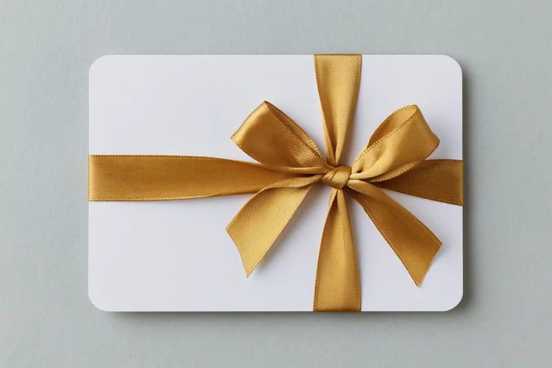 White gift card with gold ribbon bow on plain surface
