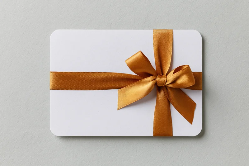 White gift card with rounded corners wrapped horizontally with a gold ribbon bow