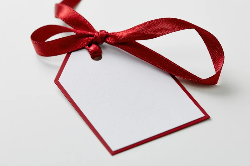 Blank white gift tag with red border and red ribbon bow on white background