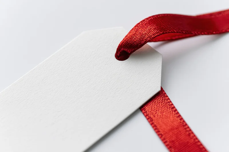 Blank white gift tag with red satin ribbon threaded through hole on plain white background
