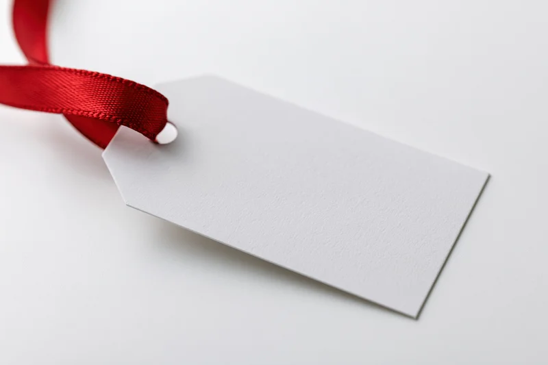 Blank white gift tag with red satin ribbon on white background