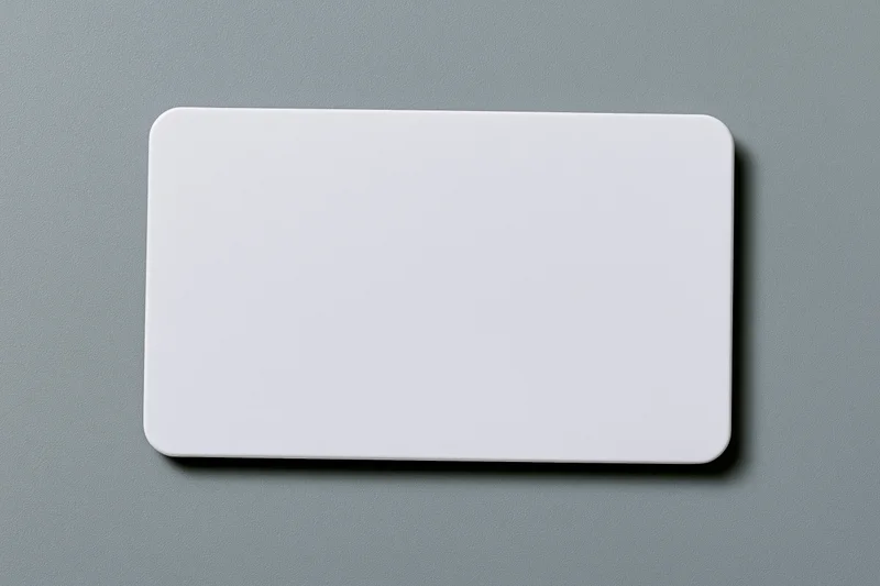 Blank white plastic card with rounded corners lying flat on a gray textured surface