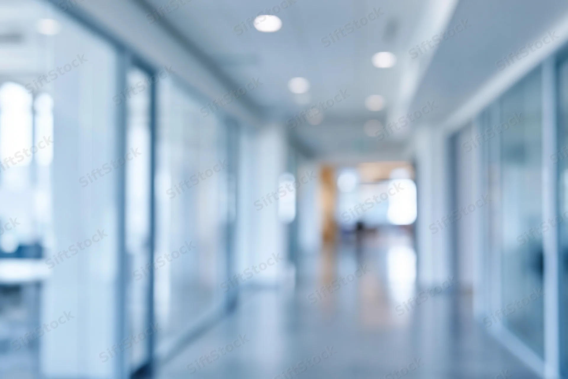 Blurred view of a modern office corridor with glass walls and recessed ceiling lights