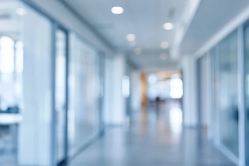 Blurred view of a modern office corridor with glass walls and recessed ceiling lights