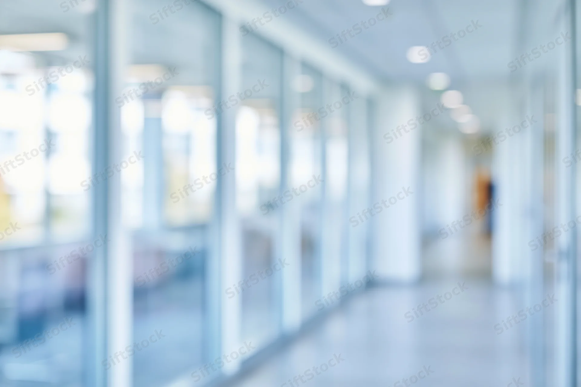 Blurred view of a modern office corridor with glass partitions and ceiling lights