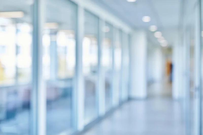 Blurred view of a modern office corridor with glass partitions and ceiling lights