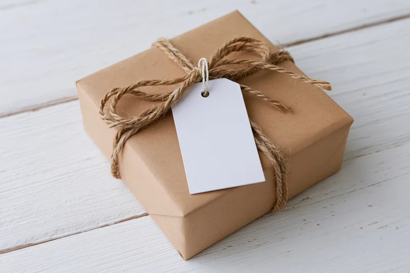 Brown kraft paper gift box tied with natural twine and blank white tag on white wooden surface