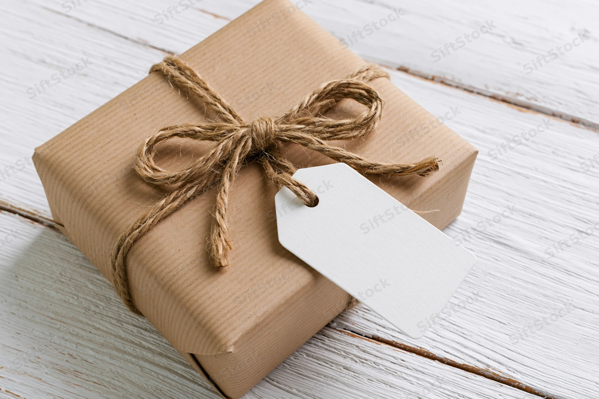 Brown kraft paper gift box tied with natural twine and blank tag on white wooden surface