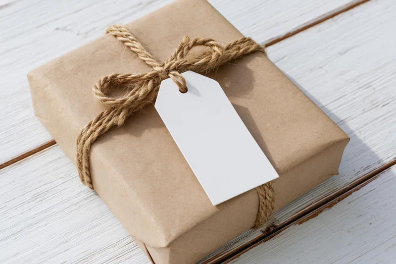 Brown kraft paper gift box tied with natural twine and blank white tag on white wooden surface