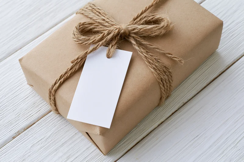 Brown kraft paper gift box tied with natural twine and blank white tag on white wooden surface