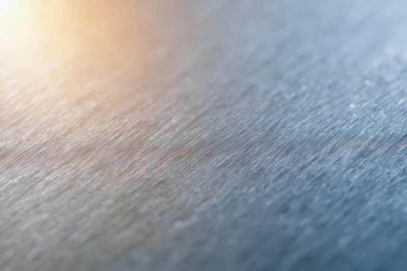 Close-up of brushed metal surface with soft light reflections and textured grain