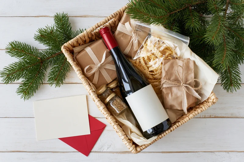 Christmas gift basket with wine, wrapped gifts, and pine branches on white wooden table
