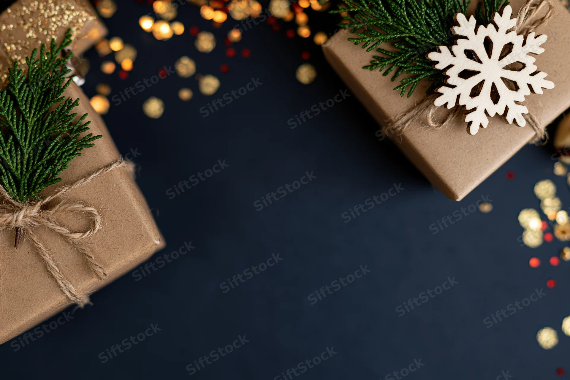 Christmas gift boxes wrapped in brown kraft paper with twine and evergreen sprigs on navy background with gold bokeh lights and confetti