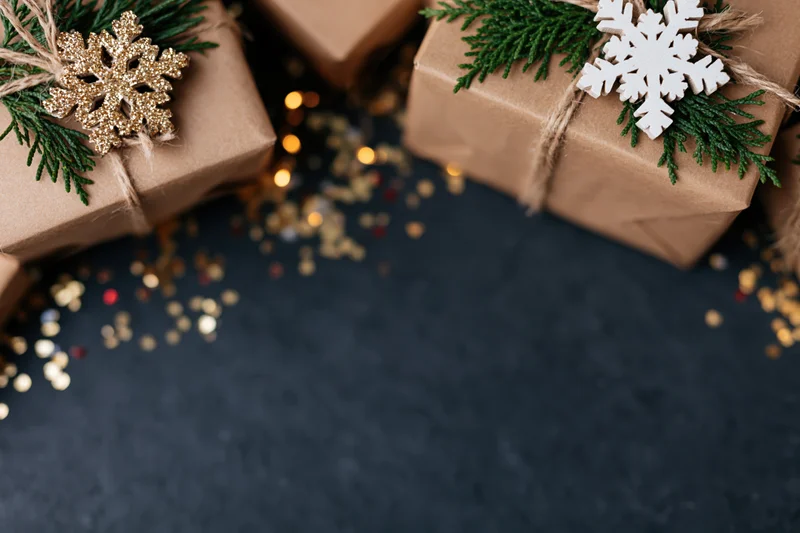 Christmas gift boxes wrapped in brown kraft paper with snowflake and evergreen decorations on dark surface