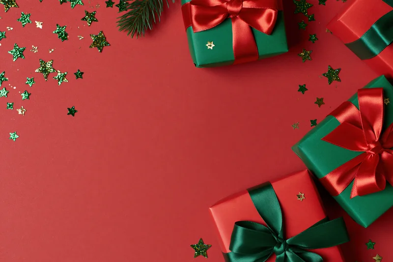 Christmas gift boxes wrapped in red and green paper with satin ribbons and glitter stars on a red surface