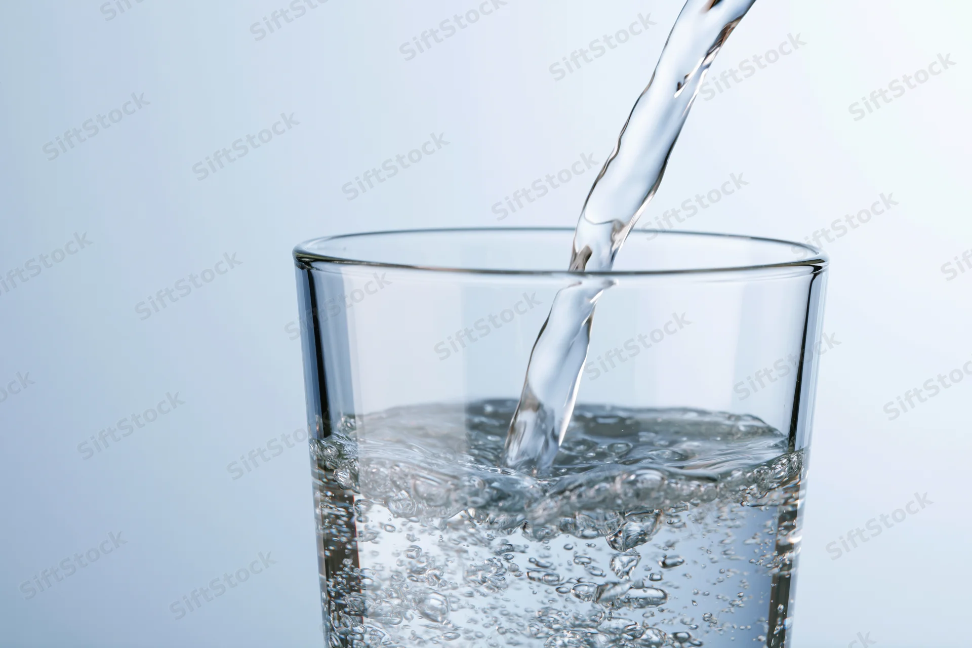 Clear water being poured into a tall drinking glass against a light blue background