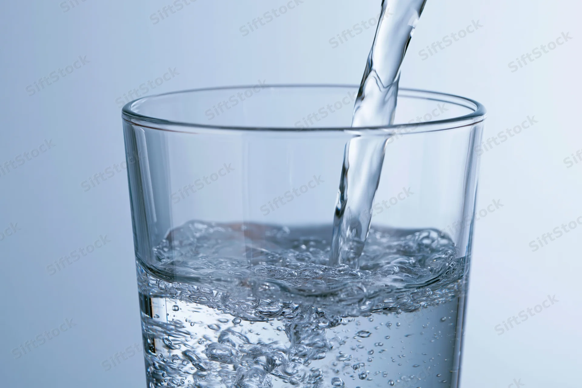 Water being poured into a tall glass against a light blue background