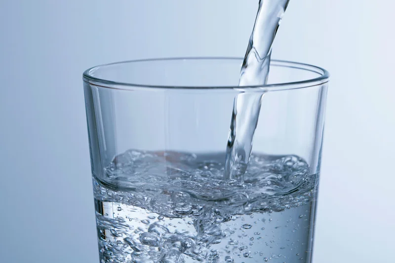 Water being poured into a tall glass against a light blue background