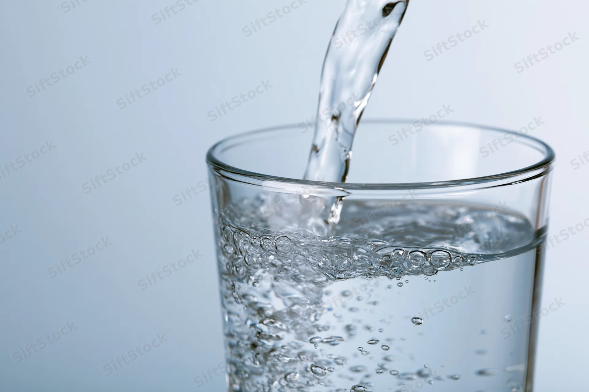 Clear water being poured into a tall drinking glass against a light blue background