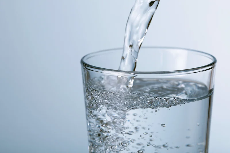 Clear water being poured into a tall drinking glass against a light blue background