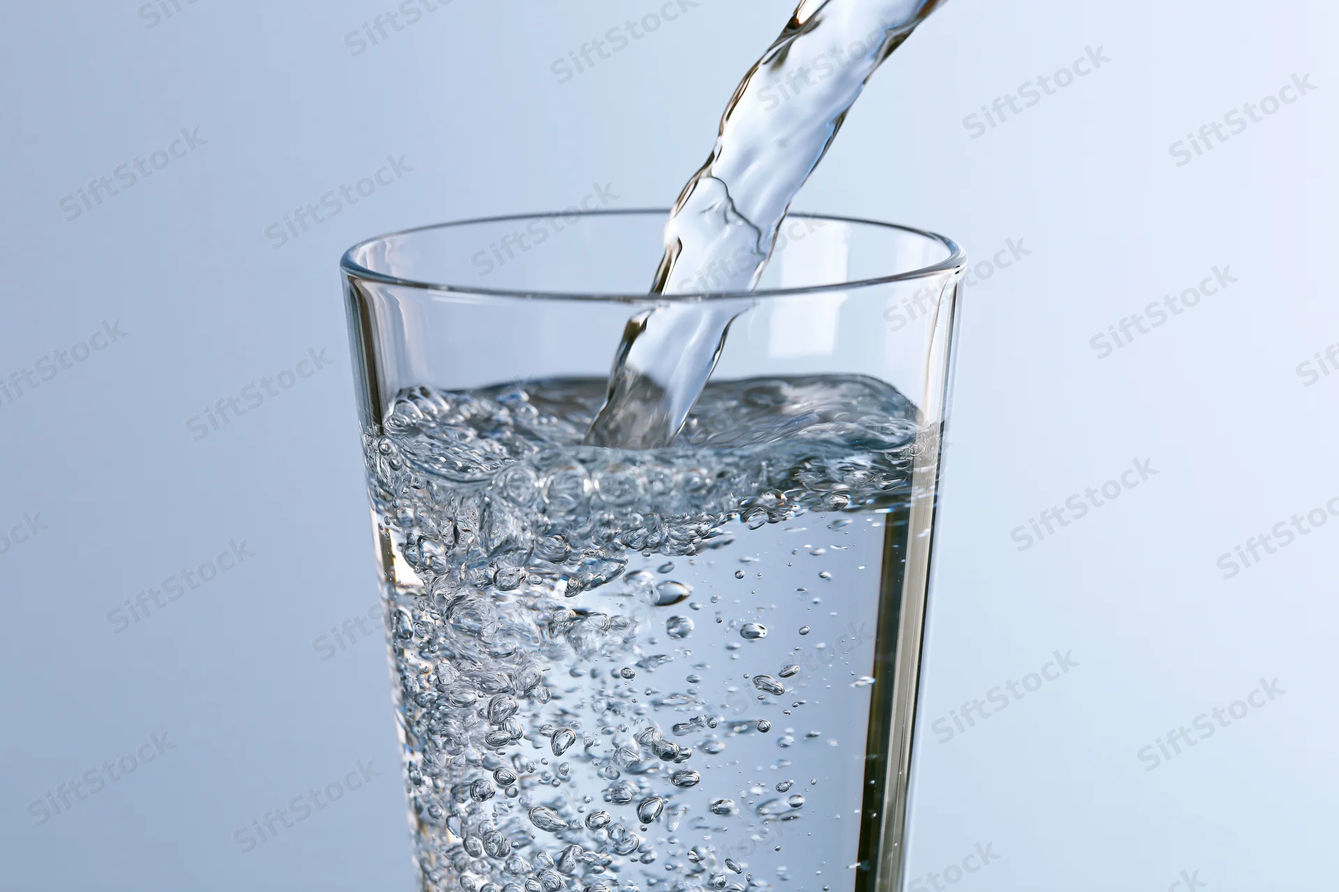Clear water being poured into a tall drinking glass against a light blue background