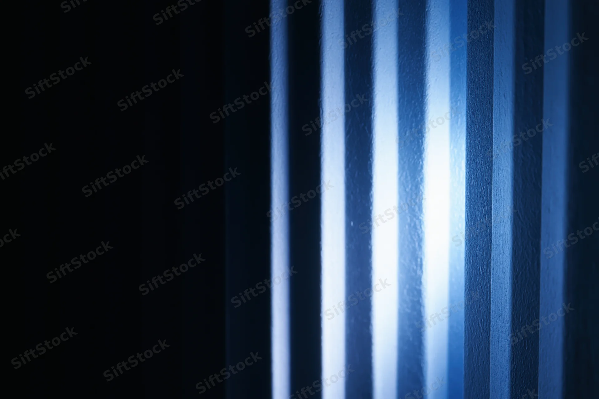 Vertical ridged panels illuminated by blue light casting shadows on a dark surface