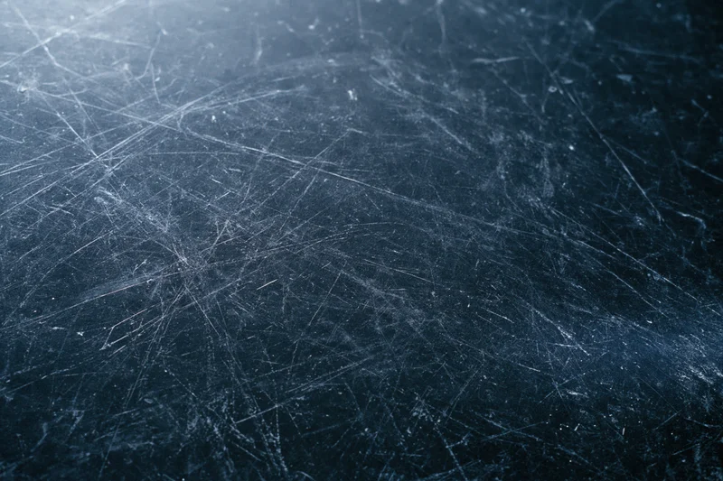 Close-up of a dark scratched metal surface with visible wear and scuff marks