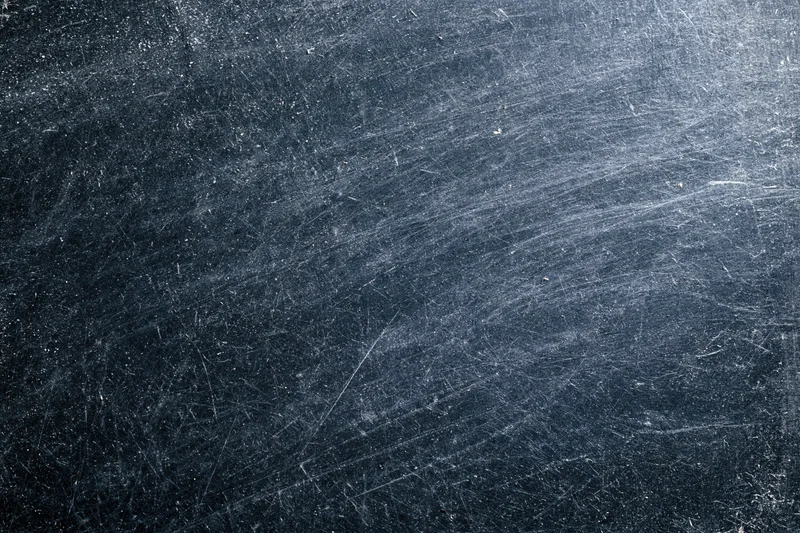 Close-up of a dark scratched metal surface with visible wear and texture