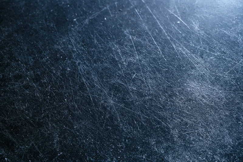 Close-up of a dark scratched metal surface with visible wear and texture