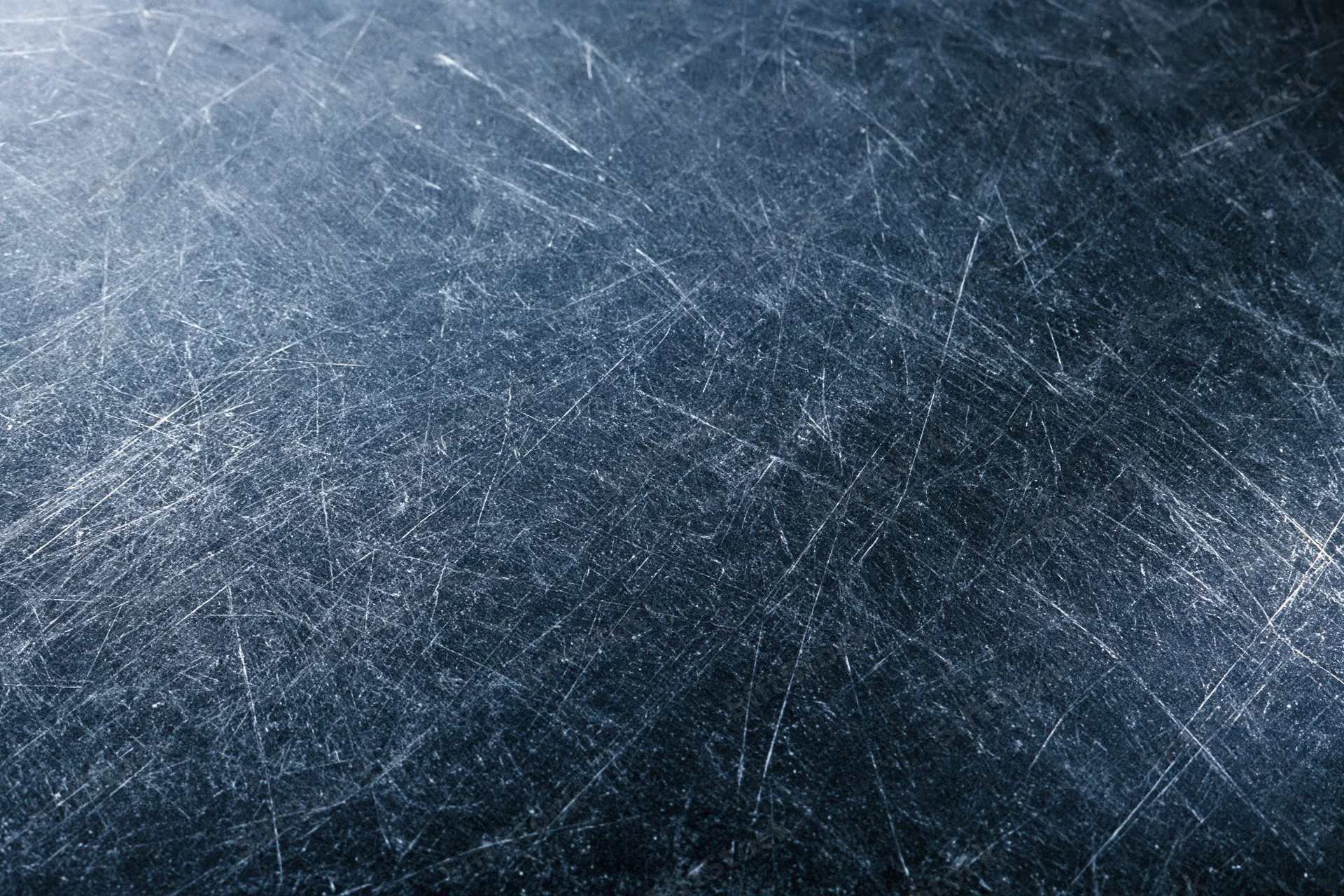 Close-up of a dark scratched metal surface with visible wear and texture