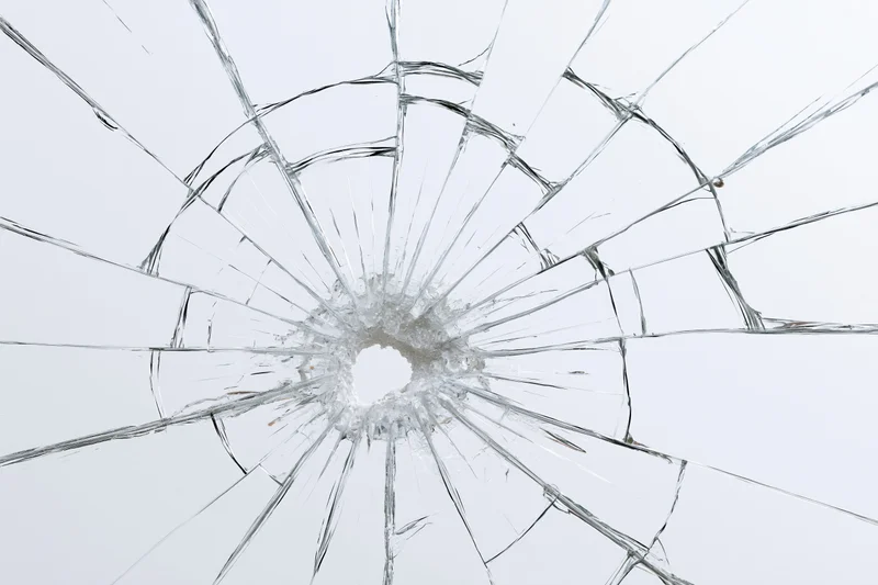 Shattered glass with radial cracks and central hole on white background