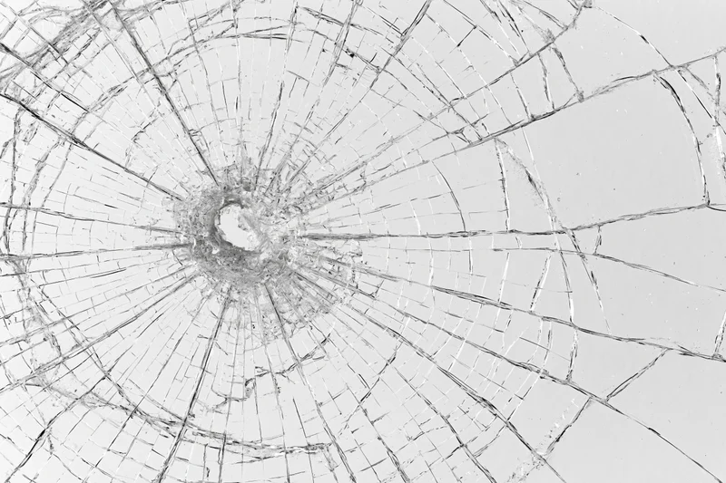 Close-up of shattered glass with radial cracks spreading from central hole