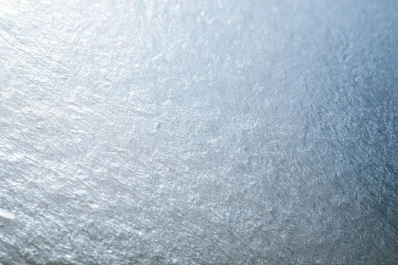 Close-up of frosted glass or brushed metallic foil surface with textured sheen and light gradient
