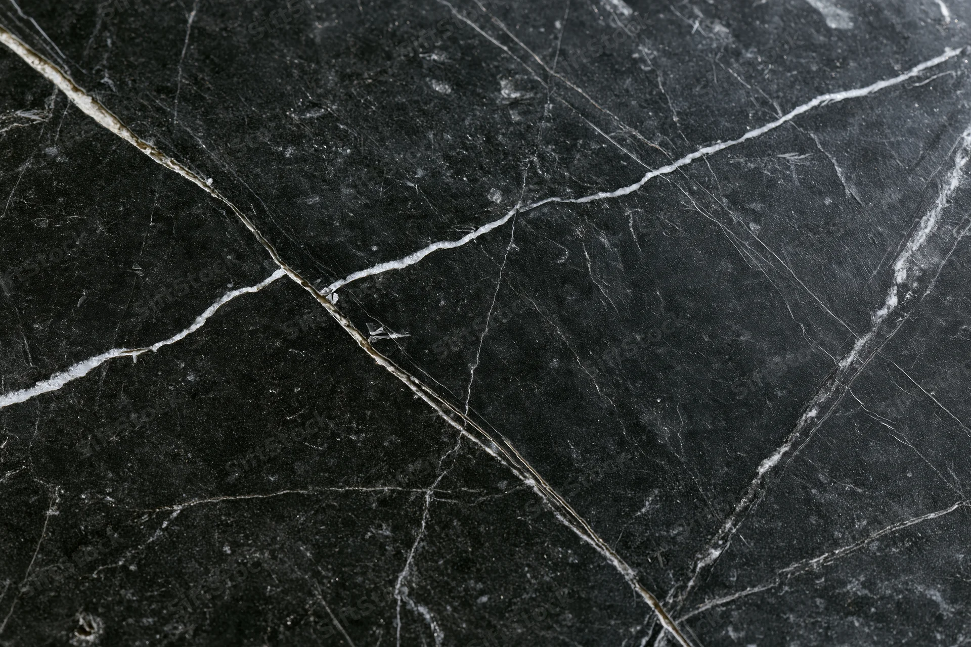 Close-up of polished black marble surface with white veining and natural cracks
