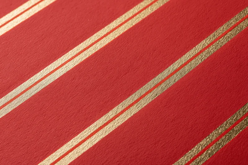 Close-up of red wrapping paper with diagonal gold and white stripes for gift wrapping