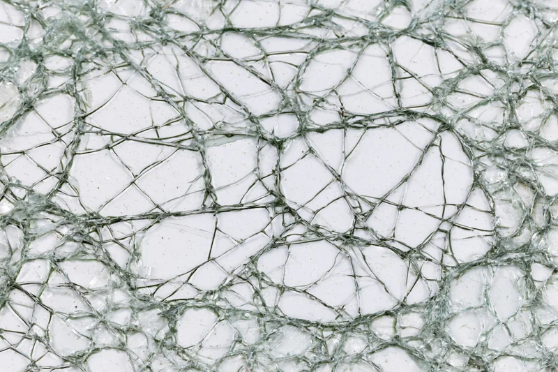 Close-up of shattered glass surface showing dense spiderweb cracks and fragments
