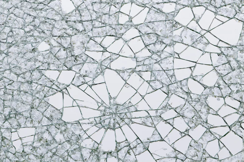 Close-up of shattered glass surface with spiderweb cracks radiating from center